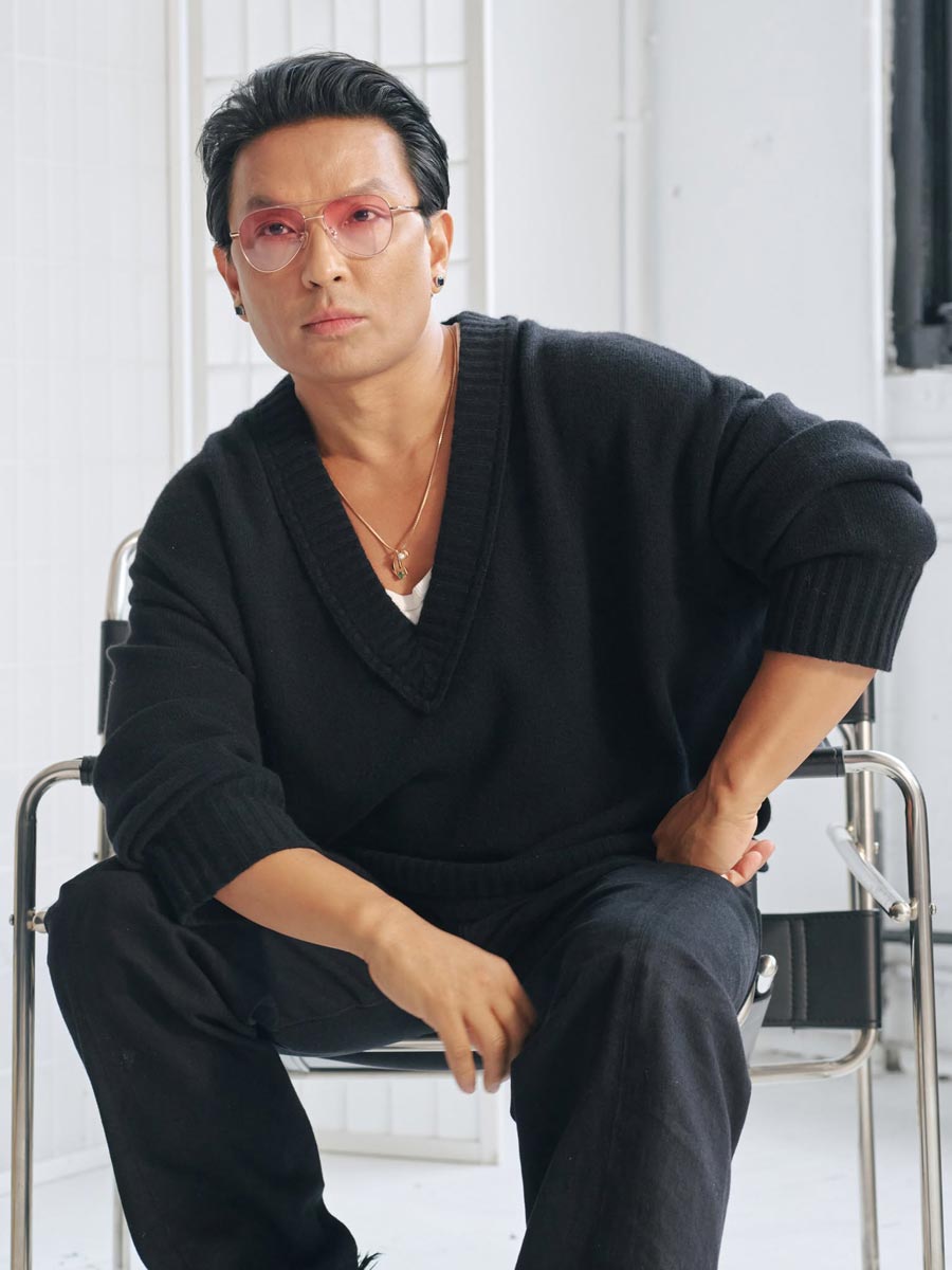 Prabal Gurung sitting in a chair, posing confidently while showcasing the ZEELOOL exclusive eyewear collection.