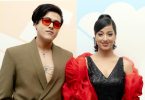 Riyan Giri wearing red sunglasses and a blazer stands beside debut actress Pratima Thapa in a black dress with red sleeves, posing at a film announcement event.