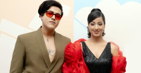 Riyan Giri wearing red sunglasses and a blazer stands beside debut actress Pratima Thapa in a black dress with red sleeves, posing at a film announcement event.