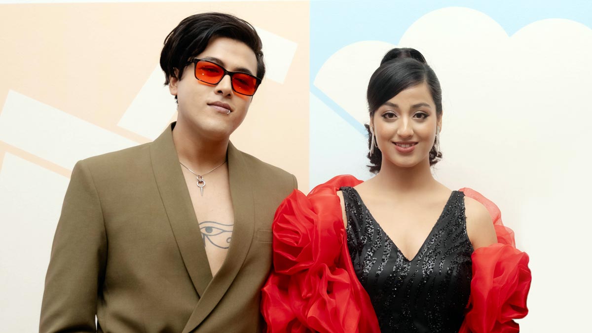 Riyan Giri wearing red sunglasses and a blazer stands beside debut actress Pratima Thapa in a black dress with red sleeves, posing at a film announcement event.