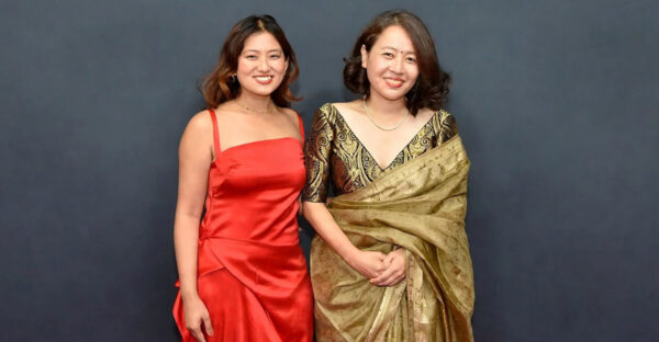Shape of Momo actress Gaumaya Gurung in a red dress stands beside director Tribeny Rai in a gold sari.
