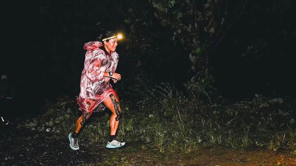 Priya Rai running along a dark forest trail in a headlamp and translucent rain poncho during the Lingjiu Mountain ultramarathon in China.