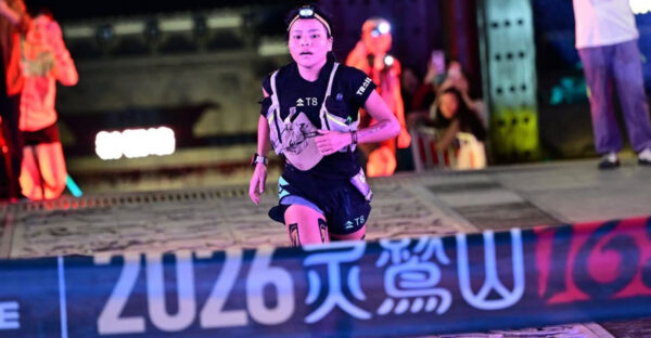 Priya Rai wearing a headlamp and hydration vest as she approaches the finish banner at the Lingjiu Mountain ultramarathon in China at night.