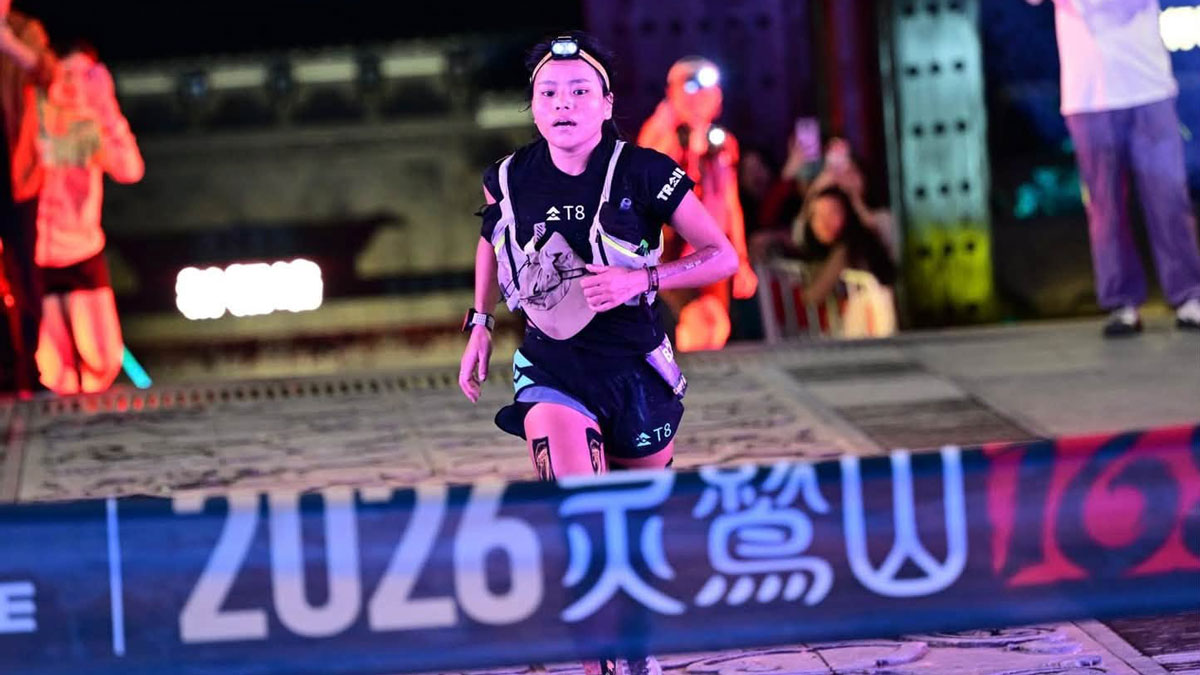 Priya Rai wearing a headlamp and hydration vest as she approaches the finish banner at the Lingjiu Mountain ultramarathon in China at night.