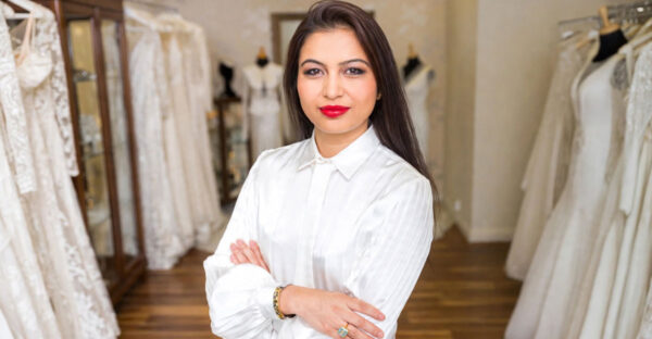 Sanyukta Shrestha wearing a white blouse with her arms folded, surrounded by wedding dresses in a bridal boutique.