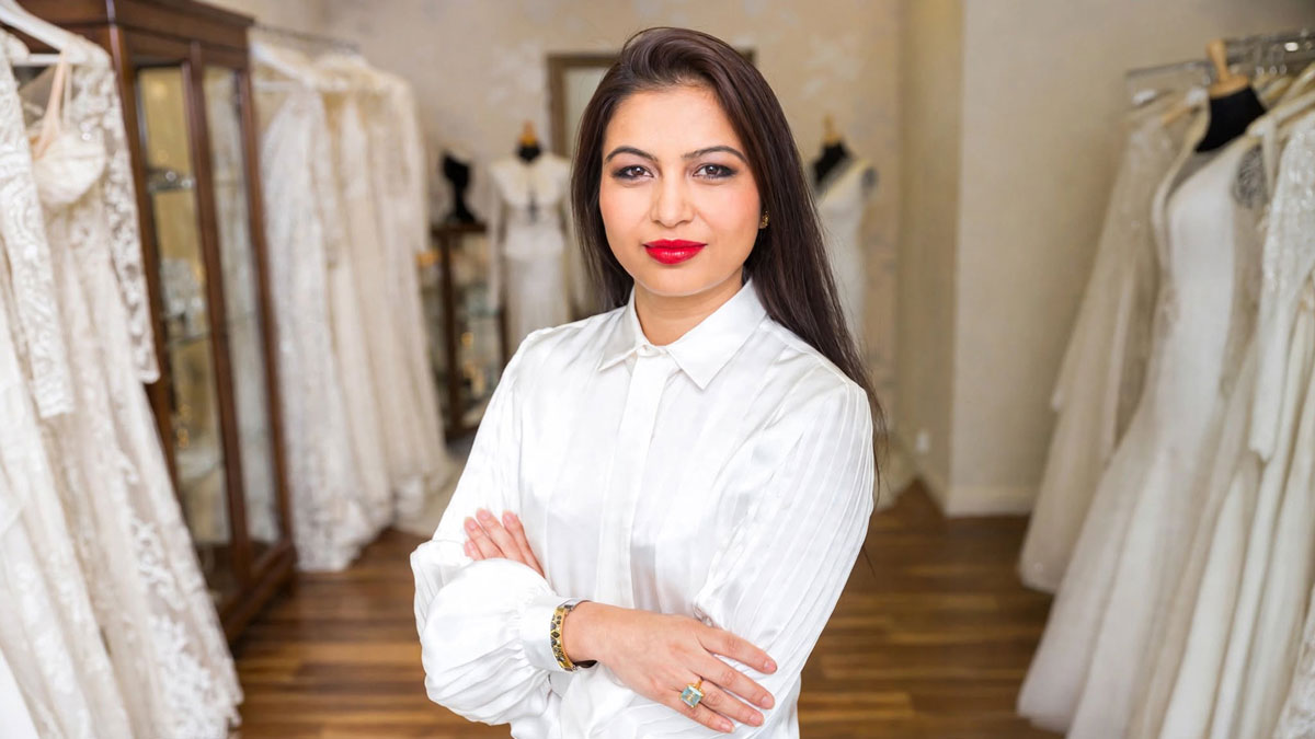 Sanyukta Shrestha wearing a white blouse with her arms folded, surrounded by wedding dresses in a bridal boutique.