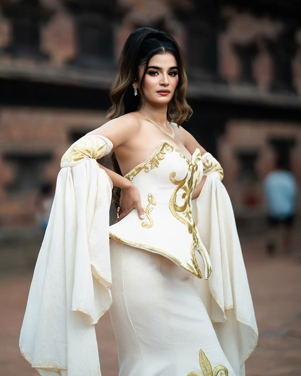 Model wearing an ivory mermaid gown with gold motifs, a sculpted corset and long flowing sleeves before a carved gateway.