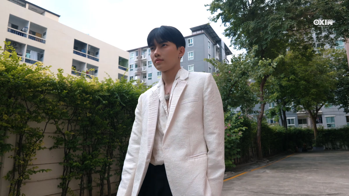 Siddhartha Tamang in a white blazer and black trousers on an outdoor driveway, with trees and buildings behind him.